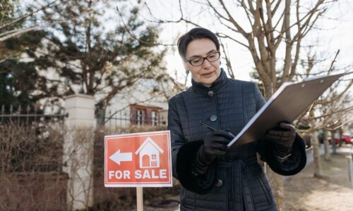 A real estate agent reviews a clipboard next to a 'For Sale' sign outside a property on a clear day. - Photo by Pavel Danilyuk on Pexels