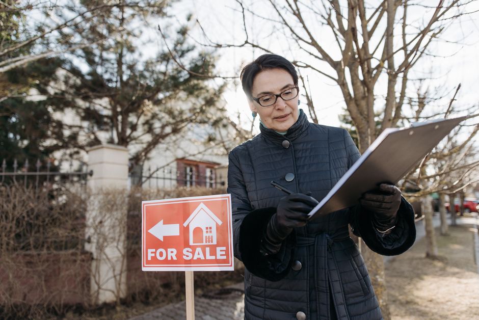 A real estate agent reviews a clipboard next to a 'For Sale' sign outside a property on a clear day. - Photo by Pavel Danilyuk on Pexels