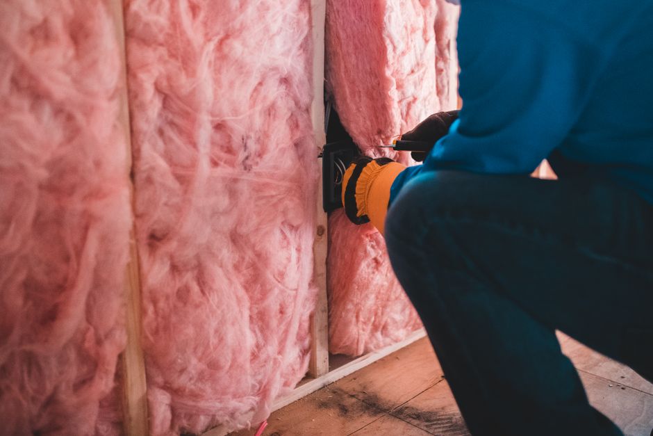 Crop unrecognizable worker in gloves sitting on haunches and insulating with pink stone wool - Photo by Erik Mclean on Pexels