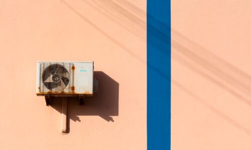 Rusty air conditioning unit casting shadow on a peach wall with blue stripe. - Photo by Jan van der Wolf on Pexels
