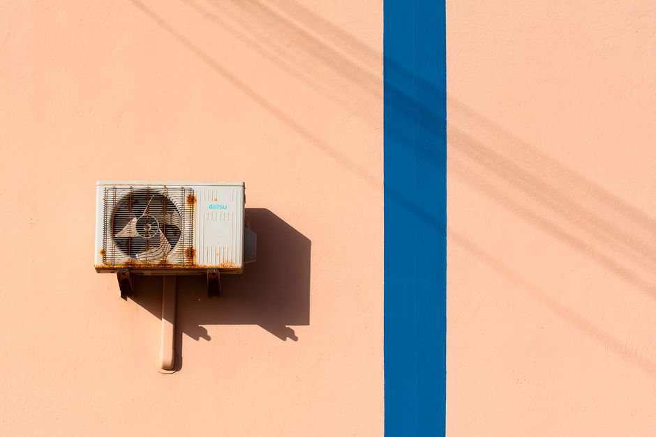 Rusty air conditioning unit casting shadow on a peach wall with blue stripe. - Photo by Jan van der Wolf on Pexels