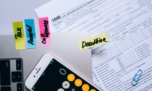 Office desk flat lay showing tax documents, calculator app on smartphone, sticky notes, and paperclips. - Photo by Leeloo The First on Pexels