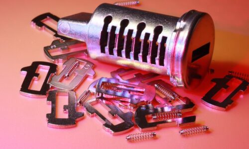 Detailed image of a disassembled lock cylinder and its metal components on a colored surface. - Photo by Nic Wood on Pexels