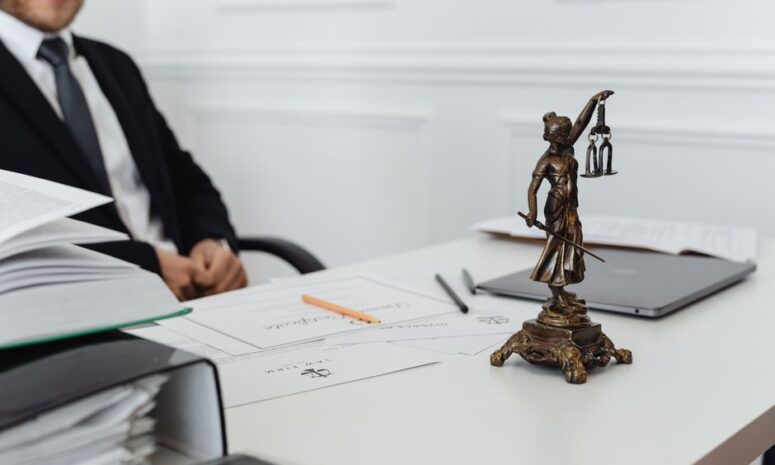 A legal professional's workspace featuring Lady Justice statue, documents, and a laptop. - Photo by https://kaboompics.com/ on Pexels