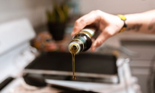 A focused image showing olive oil being poured from a bottle into a pan during cooking. - Photo by RDNE Stock project on Pexels