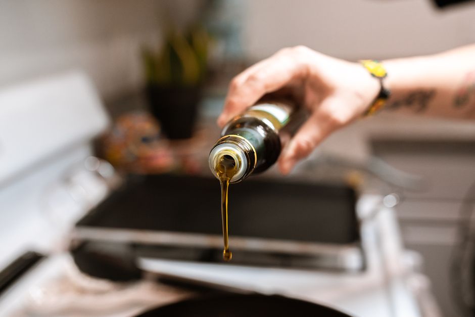 A focused image showing olive oil being poured from a bottle into a pan during cooking. - Photo by RDNE Stock project on Pexels